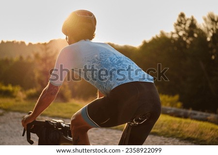 Close-up back view of a male cyclist riding a bicycle on a gravel road at sunset in the mountains.Gravel biking. Extreme sports and activity concept.Cyclist enjoying the gravel trail. Romania