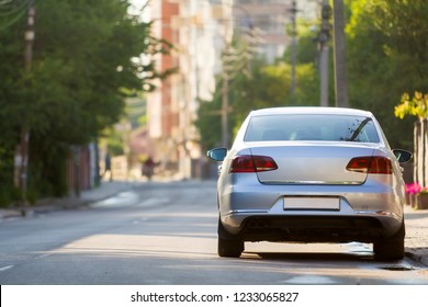 Close-up back view of new shiny expensive silver car moving along city street on blurred trees, cars and buildings background on sunny summer day. Comfortable transportation and speed in modern life.