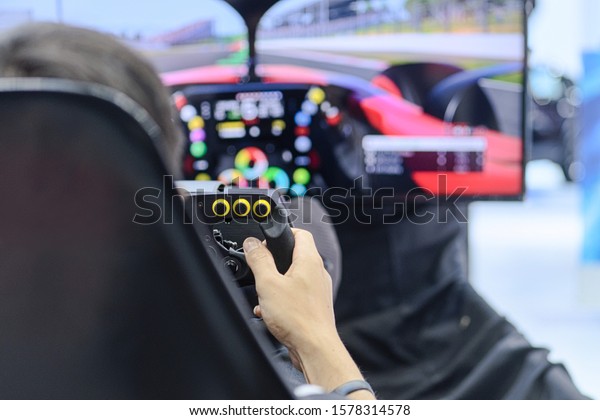Close-up from back view and selective focus right\
hands of young man gamer who enjoying with racing game via gaming\
wheel controller on gaming monitor blurred background, entertain on\
leisure, e-sport