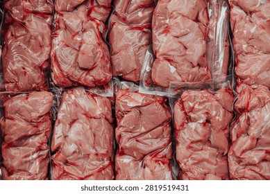 Close-up background of assorted raw beef portions tightly vacuum sealed in clear plastic bags for storage, freezing, or retail packaging