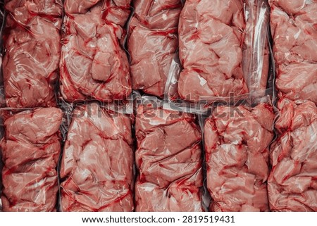 Close-up background of assorted raw beef portions tightly vacuum sealed in clear plastic bags for storage, freezing, or retail packaging
