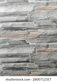 A close-up background texture of wall ceramic tiles featuring a realistic faux stone cladding pattern in natural shades of grey, beige, and brown for modern home interior design.