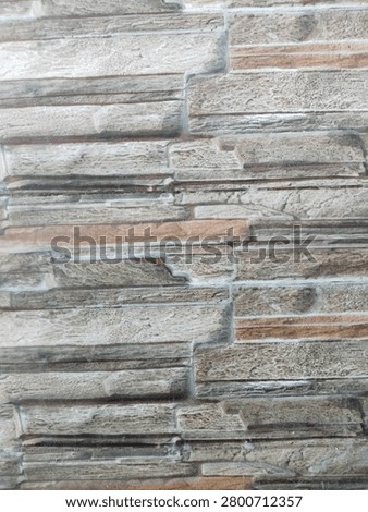 A close-up background texture of wall ceramic tiles featuring a realistic faux stone cladding pattern in natural shades of grey, beige, and brown for modern home interior design.