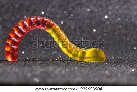 Close-up of a backlit red-yellow gummy worm crawling against a glittering background.