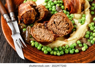 close-up of baked faggots served with creamy mashed potatoes, green peas and rich, thick onion gravy on a clay plate