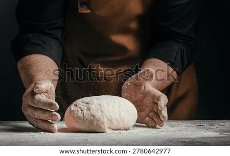 Closeup of baker hands shaping raw dough on floured table with dark background. Artisan baking process, dramatic light, copy space.