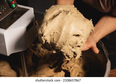 Close-up Of Baker's Female Hands Holding Dough Against The Background Of A Production Dough Mixer In A Bakery