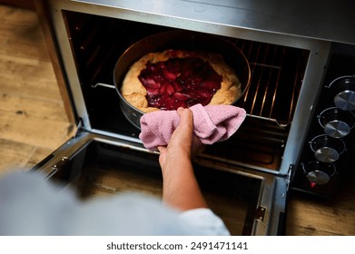 Close-up of a baker's hand removing a homemade berry pie from the oven using a pink cloth. Perfect for concepts of home baking, food, and dessert preparation. - Powered by Shutterstock