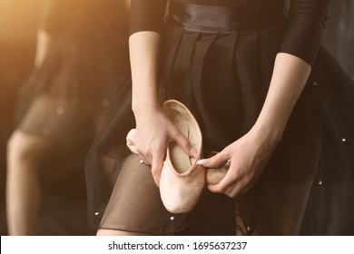 Close-up. Ballerina in a black skirt and holding a pink Pointe shoes. Sunset light in the picture
