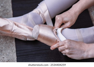 Closeup of a ballerina sitting on the floor, adjusting pointe shoe pads for foot protection during the dance. Ballet dancer putting on toe pads on her feet before performing - Powered by Shutterstock