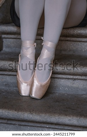 Closeup of ballerina's legs with her pink pointes shoes on. Ballet dancer is sitting on the gray stone steps. Dancer is resting on the stair. Dancer´s feet with pink ballet slippers on. 