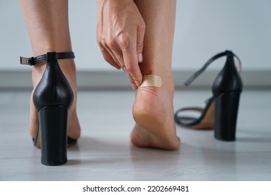 Closeup of band-aid on blister on leg. Woman having pain after wearing high heeled tight shoes. Female using bactericidal medical adhesive plaster. Foot skin care, prevention of corns and calluses.