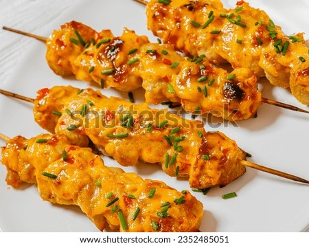 close-up of Bang Bang Chicken Kabobs sprinkled with chives on white plate on white wooden table, dutch angle