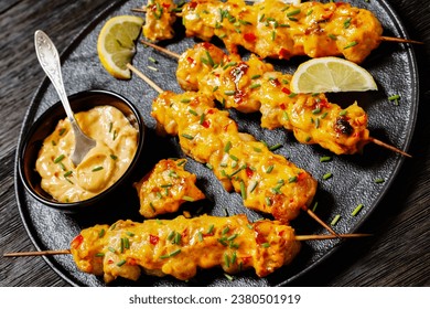 close-up of Bang Bang Chicken Skewers sprinkled with chives and lemon slices on black plate on dark wooden table, dutch angle