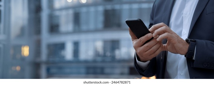 Closeup banner shot of business man hands using app holding smartphone cellphone at office building. Male entrepreneur businessman in formal suit working in trading on mobile cell phone, copy space - Powered by Shutterstock