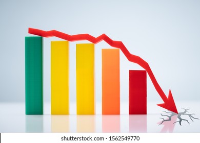 Close-up Of Bar Graph And Downward Arrow Showing Crisis In Business Concept On Reflective Table