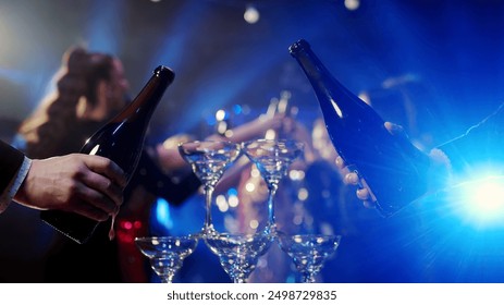 Close-up of a bar riser, the bartender pours champagne. A group of happy people at a party celebrating and drinking champagne in a club, against the backdrop of bright lights. - Powered by Shutterstock