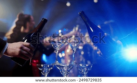 Close-up of a bar riser, the bartender pours champagne. A group of happy people at a party celebrating and drinking champagne in a club, against the backdrop of bright lights.