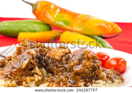 Closeup of Barbecue Meatballs on rice covered with spicy BBQ Sauce.  On red tablecloth with hot peppers in background.