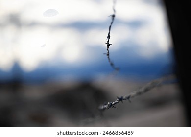 Close-up of barbed wire with a blurred background of blue sky and distant landscape. - Powered by Shutterstock