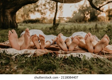 close-up bare feet of whole family resting. cheerful happy family dad mom daughters lay laying on grass picnic plaid have fun at summer outdoors together. father mother sisters parents barefoot people