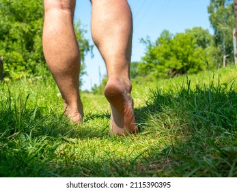 Close-up Of Bare Male Feet Walking On The Grass In The Village In Summer.