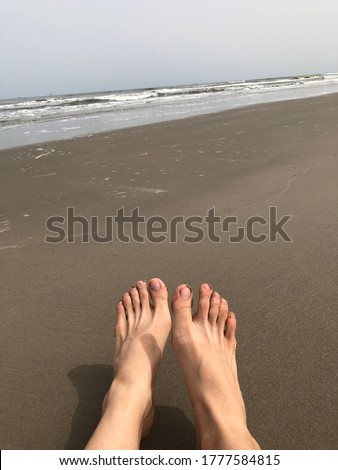 Closeup of a woman’s barefoot with brown fine skin on a beach with the sea in the background. She doesn’t paint her nails and needs pedicure. It shows relaxation, vacation, alone, sunbathing, outdoor.