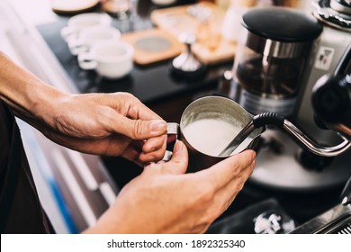 Close-up barista hands frothing warm milk on a coffee machine for making cappuccino or latte coffee in a coffee shop. - Powered by Shutterstock