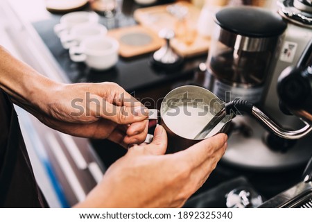Close-up barista hands frothing warm milk on a coffee machine for making cappuccino or latte coffee in a coffee shop.