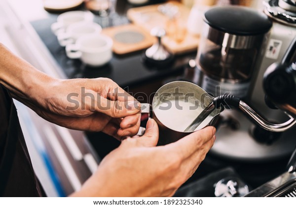 Close-up\
barista hands frothing warm milk on a coffee machine for making\
cappuccino or latte coffee in a coffee\
shop.