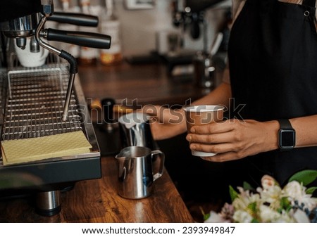 Close-up of a barista's hands pouring frothed milk into a paper coffee cup, with a blurred espresso machine in the background [[stock_photo]] © 