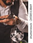 Close-up of a bartender expertly pouring gin over ice in a cocktail glass, garnished with fresh berries