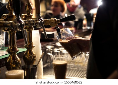 closeup of a bartender pouring a dark stout beer in tap behind the bar counter
