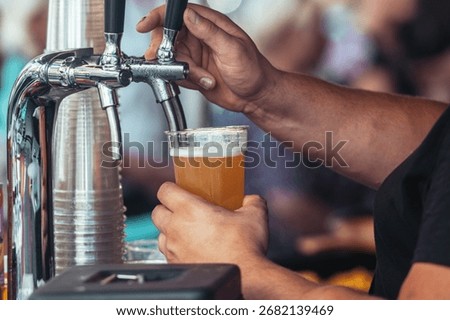 Close-up of a bartender pouring fresh draft beer into a plastic cup at an outdoor festival. Cold foamy lager being served from a tap, symbolizing refreshment, brewing, and celebration