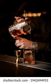 Close-up Of Bartender's Hand Holds Crystal Mixing Cup With Cold Cocktail And Pours It Through Sieve Into Old-fashioned Glass On Bar Counter