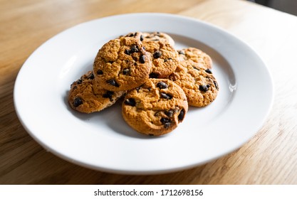 Close-up of basic drop cookies with chocolate morsels. Choc chip cookies in a white plate on a wooden table. Homemade chocolate chip cookies. Traditional handmade chewy cookies with chocolate chunk