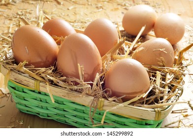 closeup of a basket with straw and a pile of brown eggs on a wooden surface - Shutterstock ID 145299892