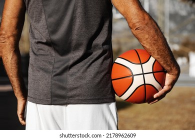 Close-up Basketball Ball In Right Hand Of Adult Man Standing Backwards Outdoor.