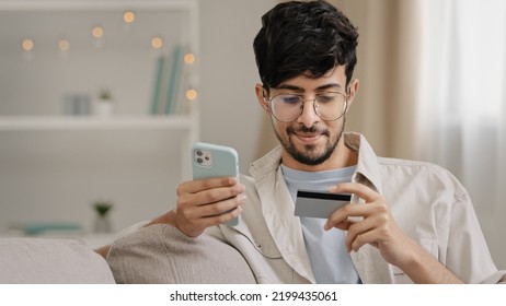 Close-up Bearded Arabic Business Man In Glasses With Credit Card And Phone Makes Purchase Online Shopping Enters Bank Number Online Transaction Uses Mobile Financial Application Booking Order Buying