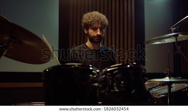 Closeup bearded\
drummer nodding head in concert hall. Expressive male musician\
playing on drum kit in recording studio. Curly hair man artist\
performing rock music\
indoors.