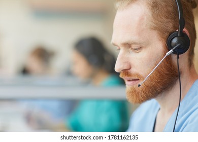 Close-up of bearded male operator using headset to talk to clients during his work in call center