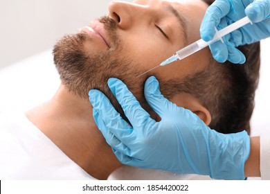 Closeup of bearded man getting beauty injection at aesthetic clinic. Plastic surgeon injecting anti-aging filler in handsome man cheeks. Male cosmetology, aesthetic medicine concept