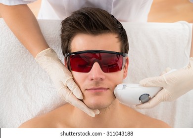 Close-up Of Beautician Giving Laser Epilation Treatment To Young Man Face