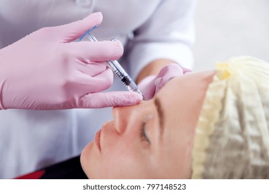 Close-up of a beautician injects Botox injection into the cheekbones of a young woman to correct the form in the medical office