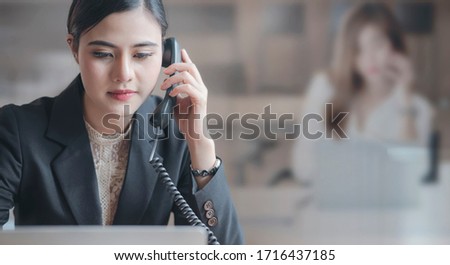 Closeup beautiful asian officer or secretary using telephone while sitting in office and working with laptop computer.