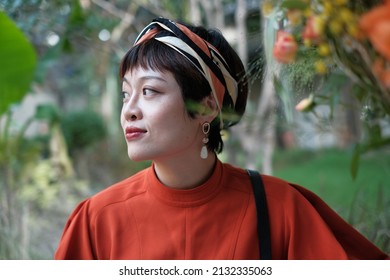 Closeup Of A Beautiful Asian Woman With Bohemia Style Hairband And Pearl Eardrops In A Garden Looking Faraway. 