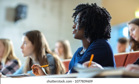 Close-up of a Beautiful Black Female Student Sitting Among Her Fellow Students in the Classroom, She's Writing in the Notebook and Listens to a Lecture.