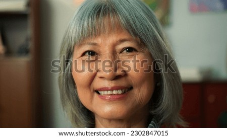 Closeup of beautiful elderly woman pretty charmingly smile looking at camera. Close up of attractive old aged female sit on couch in cozy living room. Senior Lifestyle Concept.