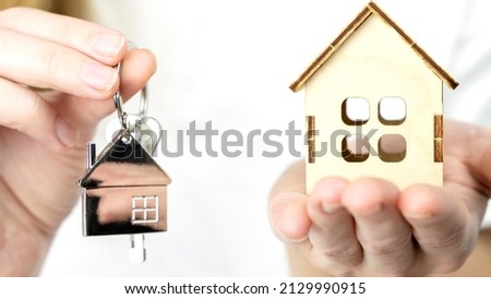 Close-up of beautiful female hands holding a key chain with a house on a blue background. Concept of dreams about your own home. Advertising space