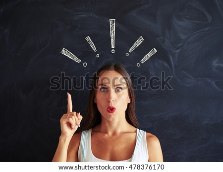 Close-up of beautiful female who look like trying to pay your attention against school blackboard with chalk exclamation marks